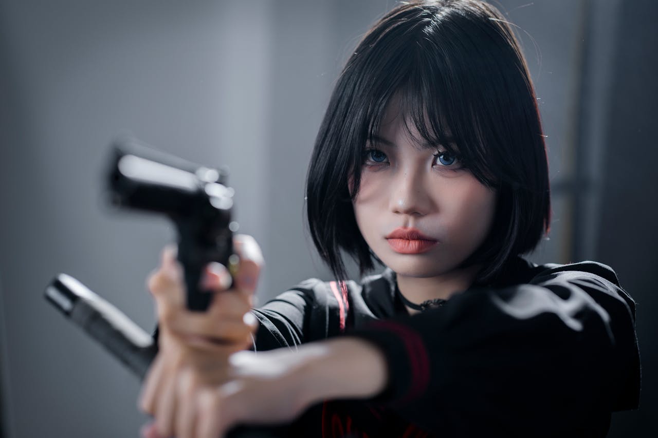 Confident young Asian woman holding and aiming a gun with focused expression.