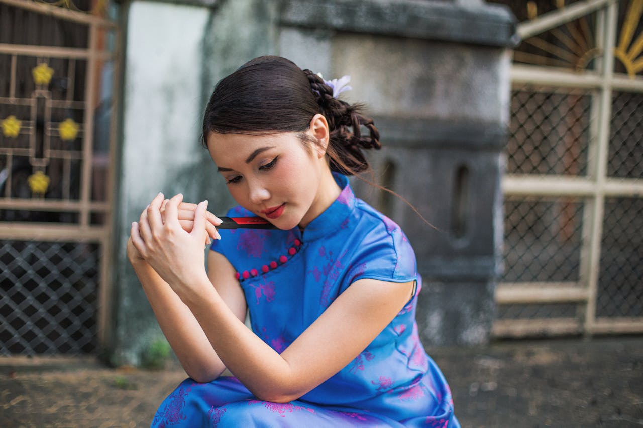 Young woman in a blue cheongsam dress, thoughtfully posing outdoors.