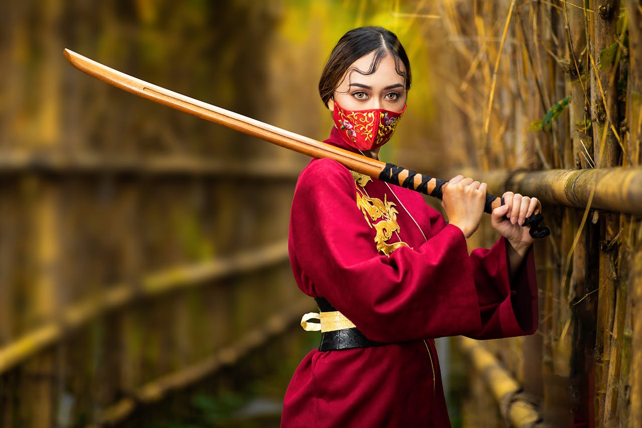 Anonymous focused female in face mask and bright wear standing with bamboo shinai on bridge while looking at camera