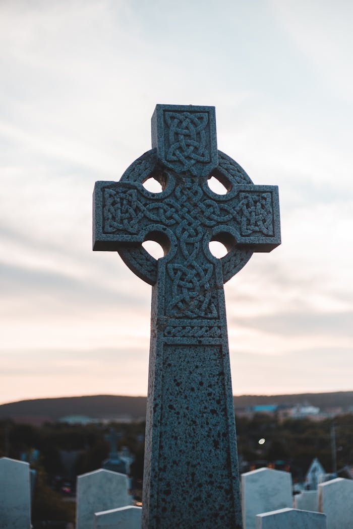 Celtic cross standing prominently against a tranquil sunset backdrop in a peaceful cemetery.